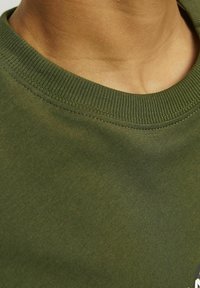 Oliven grøn t-shirt med ribbet rund hals. Glat tekstur, letvægtsstof, tæt på kraven og skulderområdet.
