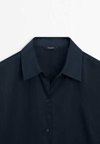 Chemise bleu marine à boutons avec col évasé, en tissu lisse ; dotée de boutons assortis et d'un design épuré et minimaliste.