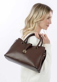 Borsa a mano in pelle marrone con un design strutturato, doppi manici superiori e un accento in oro con logo circolare. Texture liscia e base piatta.