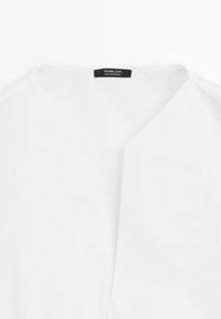 White blouse with a V-neck design, smooth texture, and clean lines. Features a tag with "Massimo Dutti" label, indicating origin from Morocco.