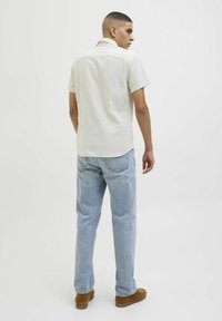 Chemise à manches courtes, de couleur claire, à texture, avec un col, associée à un jean droit bleu clair et des mocassins marron.