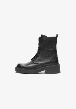 Bottine noire en cuir avec finition texturée, bout rond, design à lacets et semelle épaisse. Dotée d'une languette à l'arrière.