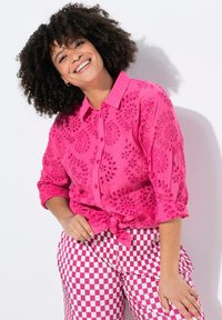 Camicia rosa brillante con dettagli ricamati e nodo in vita; abbinata a pantaloni a scacchi rosa e bianchi.