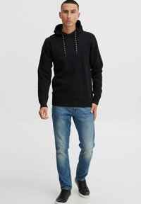Zwarte hoodie met koordjes, getailleerd ontwerp, textuurstof. Gecombineerd met lichtblauwe jeans en zwarte sneakers.