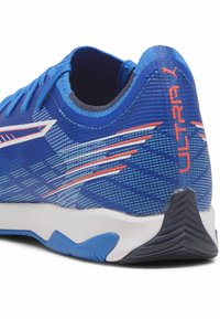Blauer Sportschuh mit orangefarbenem "ULTRA"-Text an der Ferse, weißem und orangefarbenem Streifendesign an der Seite sowie einer strukturierten blauen und schwarzen Sohle.