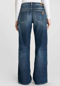 Jeans de denim azul con un diseño acampanado, que cuentan con una cintura de media altura, cinco bolsillos y una etiqueta de cuero marrón en la parte trasera.