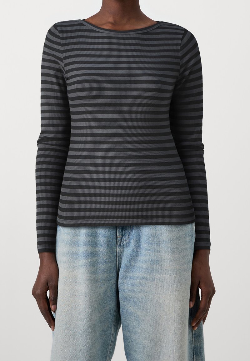 Schwarzes Langarmshirt mit abwechselnd einfarbigen und strukturierten vertikalen Streifen. Rundhalsausschnitt, figurbetonte Silhouette, kombiniert mit hellblauen weiten Jeans.