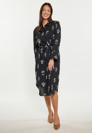 Schwarzes Hemdkleid mit weißen Blumenstickereien. Lange Ärmel, durchgehende Knopfleiste und Taillengürtel-Detail. Glattes, leichtes Material.