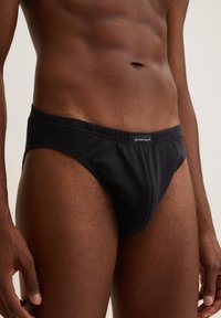 Slip bikini neri in cotone con elastico in vita. Presenta un piccolo etichetta con logo sul davanti e una texture liscia.