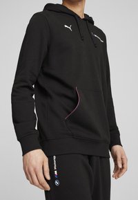 Černá mikina s kapucí vyrobená z bavlněné směsi, s bílým logem Puma, růžovým akcentem na kapse a brandingem BMW Motorsport na rukávu.