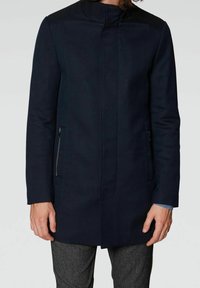 Abrigo azul marino con cuello, tela texturizada, bolsillos laterales con cremallera y diseño estilizado. Mangas largas con un ajuste entallado.