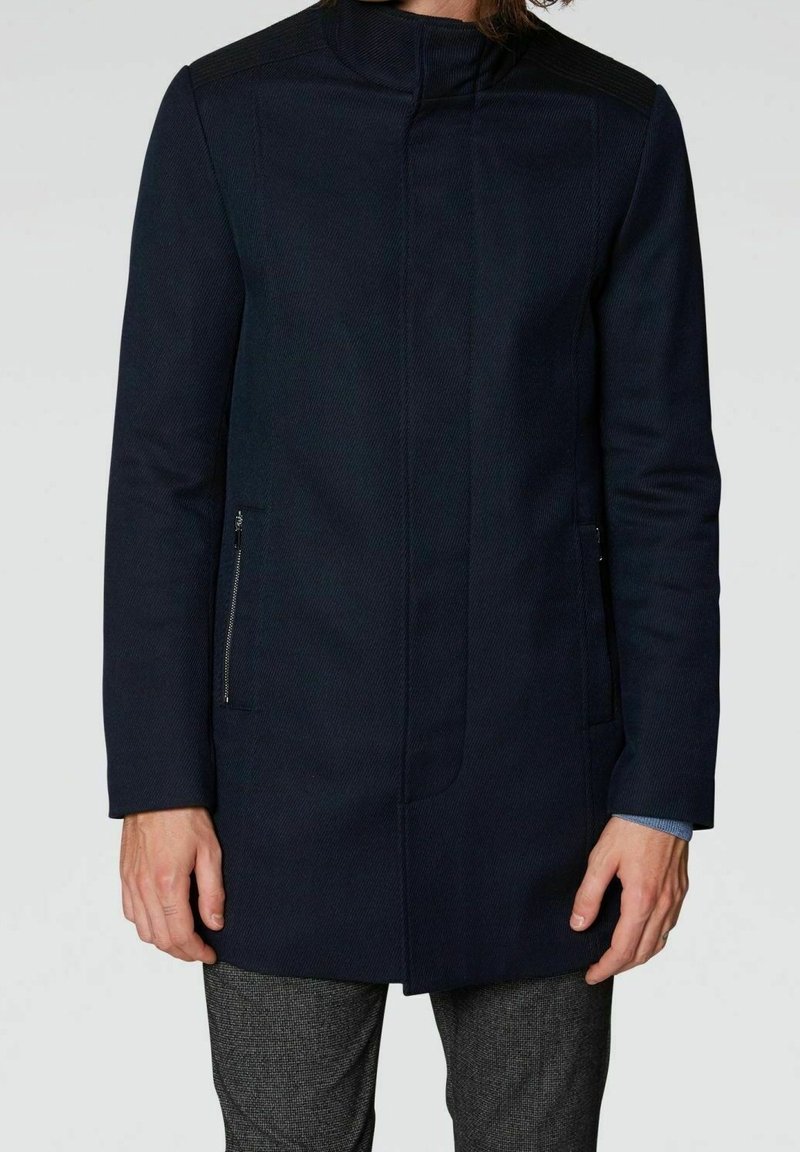 Abrigo azul marino con cuello, tela texturizada, bolsillos laterales con cremallera y diseño estilizado. Mangas largas con un ajuste entallado.