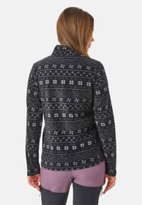 Polarowa kurtka na czarnym tle z białymi geometrycznymi i kwiatowymi wzorami. Posiada stójkę i długie rękawy.