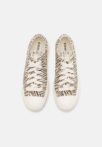 Beige Sneaker mit schwarzem Zebramuster, weißen Schnürsenkeln und einer Gummisohle. Innen mit der Aufschrift "Converse Chuck Taylor All Star" versehen.