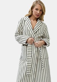 Pasiasty szlafrok w kolorze białym i czarnym, wykonany z miękkiej, fakturowanej tkaniny. Posiada kołnierz szalowy, pasek w talii oraz boczne kieszenie.
