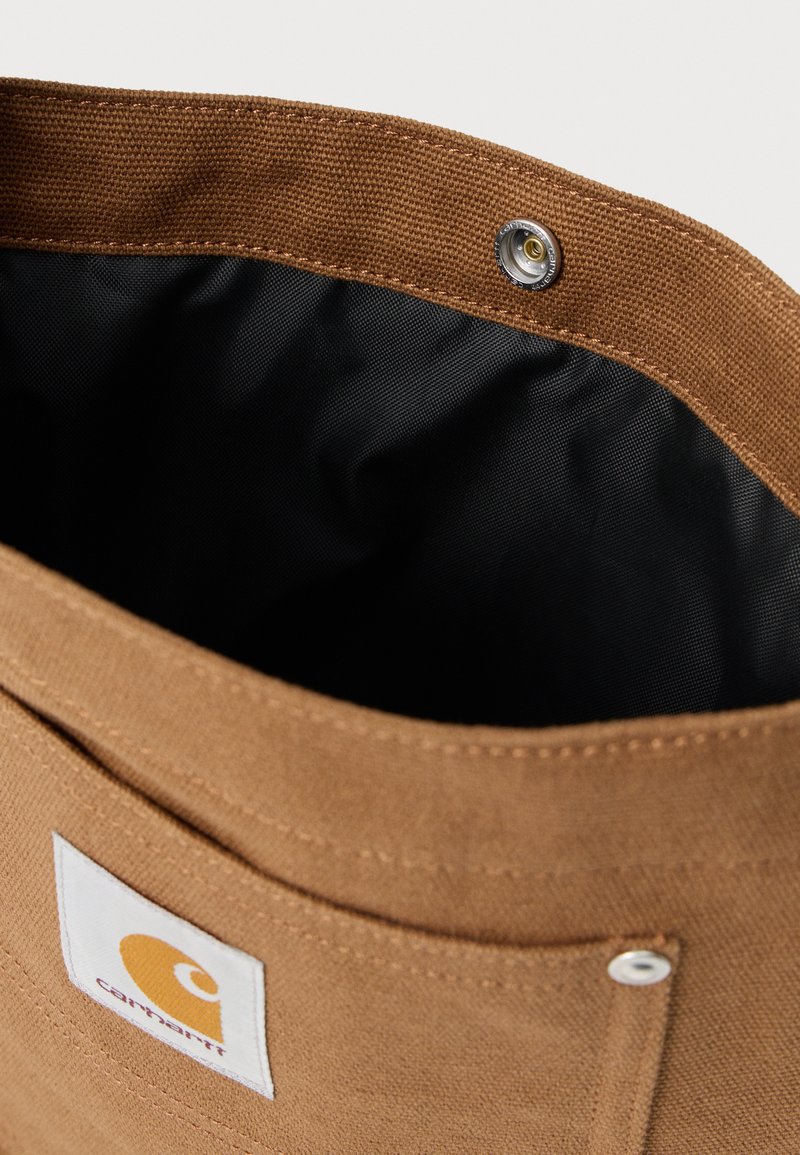 Brown Carhartt fabric bag with black interior lining and silver snap button closure.