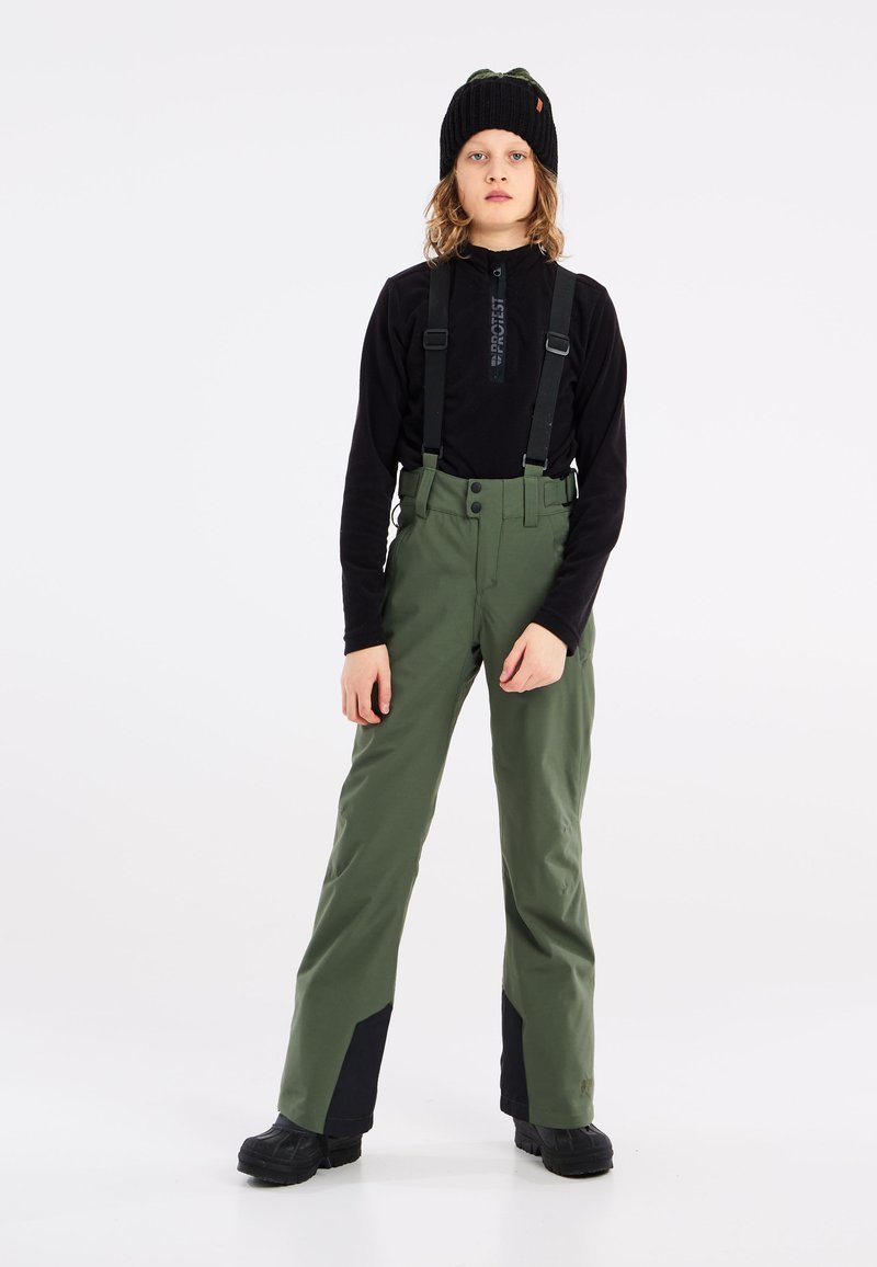 Pantalons de ski verts avec bretelles noires ajustables, poches latérales et accents noirs au bas des jambes, associés à une chemise noire à manches longues et un chapeau.