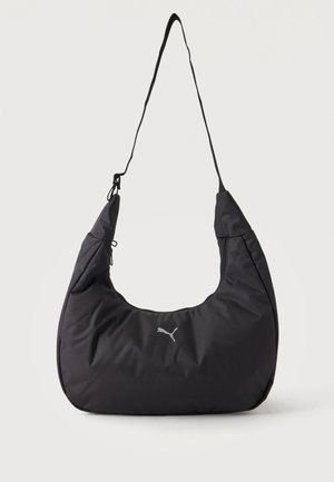 Čierna mäkká textilná taška cez rameno s nastaviteľným popruhom a malým bielym logom Puma na prednej strane na jednofarebnom svetlom pozadí.