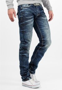 Jeans en denim bleu avec une coupe slim, texture délavée, coutures claires, poches avant et un passant de ceinture à la taille.