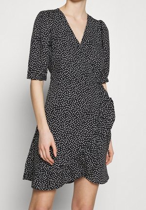 Robe noire à motif de cœurs blancs, avec un décolleté en V, de courtes manches bouffantes et un ourlet à volants en plusieurs couches. Fabriquée en tissu léger.
