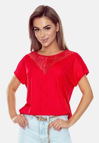 Czerwona koszulka z krótkim rękawem z koronkowym wykończeniem dekoltu. Miękki materiał, luźny krój i prosty dół. W zestawie z jasnymi dżinsami.