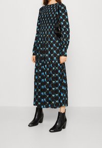 Mustapohjainen kukkamekko, jossa on sinisiä kuvioita, pitkät hihat, kerroksellinen muotoilu, yhdistetty mustiin nilkkasasutoihin, joissa on tekstuuripinta ja lohkokorko.