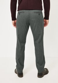 Grau strukturierte Hose mit maßgeschneiderter Passform, ausgestattet mit zwei Gesäßtaschen und dunkelbraunen Knöpfen. Kombiniert mit schwarzen Lederschuhen.