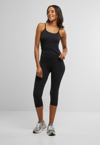 Top sport negru fără mâneci, cu bretele subțiri și o pereche asortată de colanți scurți. Materialul pare a fi neted și elastic. Fără modele notabile.