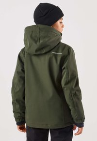Grön vattentät jacka med huva, elastiska ärmslut och en logotyp på ryggen. Bärs med en svart stickad mössa. Slät textur och modern design.