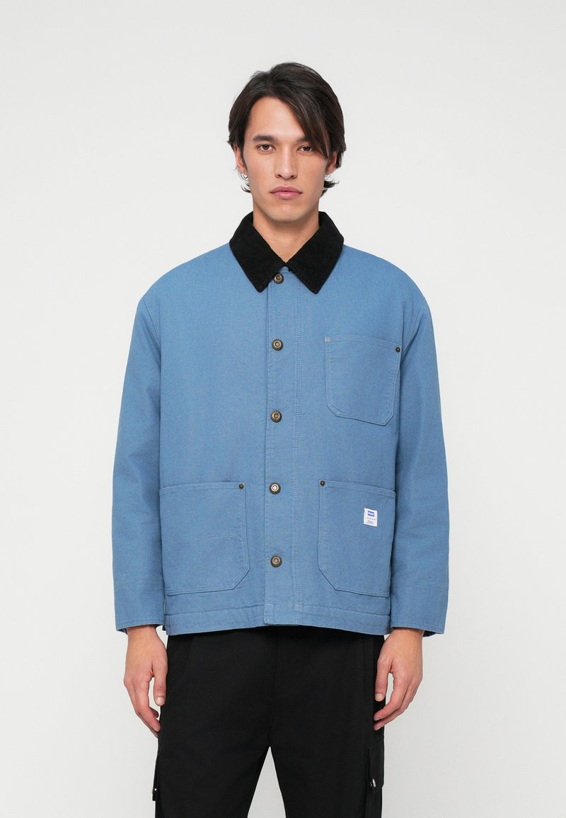 Blue work jacket with a corduroy collar, double front pockets, and brown button closures. Displayed on a neutral background.