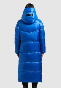 Ilgas, papūstas paltas blizgia, ryškiai mėlyna spalva, su kapišonu, siuvinėtu raštu ir dviem kišenėmis. Nugaroje yra logotipas ir užtrauktuko detalė.