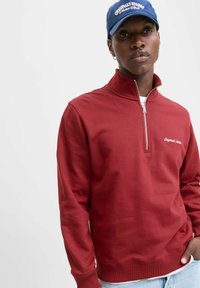 Sweatshirt rosso con zip al collo, realizzato in cotone, caratterizzato da un design aderente e polsini a coste. Include un logo bianco sul petto.