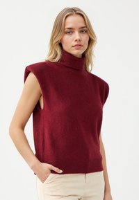 Burgundowy, bezrękawnikowy sweter w stylu golfu z miękkiej przędzy, z ribbanym wykończeniem. Oferuje otwarte otwory na ramiona i luźny krój.
