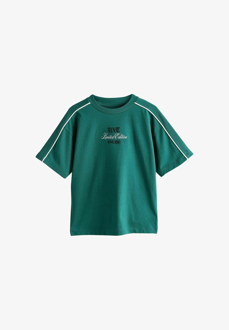 T-shirt vert à manches courtes avec passepoil blanc sur les épaules et texte brodé noir "NXT Limited Edition est. 1992" sur la poitrine.