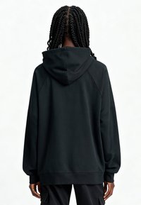 Sweat à capuche noir surdimensionné en tissu doux, doté d'une grande capuche, de manches raglan et de poignets côtelés. Texture lisse sans motifs visibles.