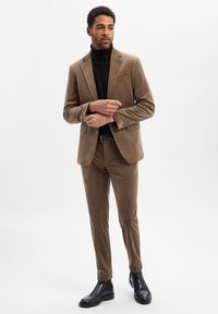 Garnitur z aksamitnego materiału w kolorze brązowym z dopasowanym krojem, zestawiony z czarnym golfem. Uzupełniony eleganckim czarnym paskiem i czarnymi botkami za kostkę.