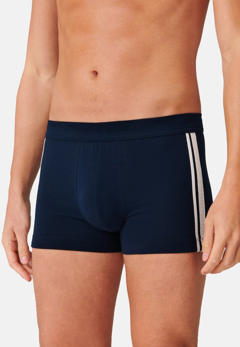 Mörkblå boxertrosa i mjukt tyg, med en figursydd passform och två horisontella vita ränder längs sidorna. Elastisk midja.