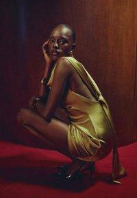 Robe en satin jaune avec un dos nu, design épuré, tissu drapé, associée à des chaussures à talons hauts noires, sur un fond rouge.