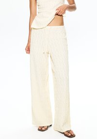 Pantalons lâches, jaune pâle, texturés avec une taille à cordon, associés à un haut assorti. Le tissu a un motif ondulé et une finition douce.