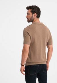 Kortärmad, ljusbrun polotröja med strukturerad stickning, ribbad krage och mudd. I kombination med mörka jeans, set bakifrån.