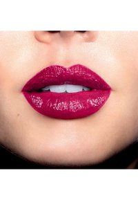 Diep bessenkleurige lipstick op volle lippen, met een glanzende afwerking. Gladde textuur met zichtbare lichtreflectie en heldere tanden eronder.