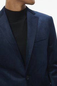 Tumesinise seemisnahast bleiser ühe nupuga kinnitusega ja rinnataskuga, kantud musta kõrge kaelusega kampsuni peal. Siidine tekstuur ja kujundatud lõige.