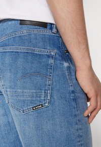 Blauwe spijkerbroek met een recht model, voorzien van een zwart leren logo patch op de achterste tailleband en een gestikte detail op de achterzak.