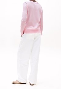 Helles rosa Sweatshirt mit langen Ärmeln, runder Ausschnitt, kombiniert mit weißen, weit geschnittenen Hosen und beigen Slippern. Glatte Textur.