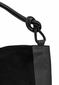 Sac à main en cuir noir et en daim avec une finition texturée. Il présente une sangle nouée et un design épuré. Les matériaux opposés créent un contraste.
