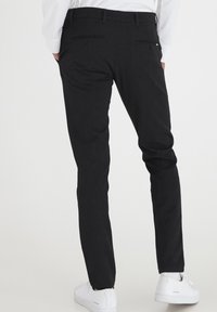 Svarta byxor med slim-fit, som har två bakfickor och en ren design. Kombineras med vita sneakers för en avslappnad look.