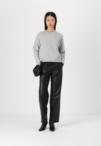 Siva pletena pulover z okroglo ovratnikom, v kombinaciji z visokim črnim hlačami iz umetnega usnja. Model drži črn clutch.