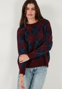Pull en tricot bordeaux et bleu marine avec un motif en losanges, doté de poignets et d'un ourlet côtelés. Texture douce adaptée au temps frais.