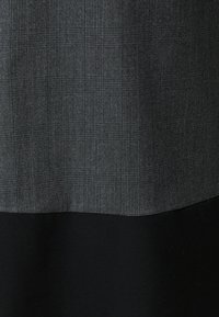 Karierter Stoff in Grautönen oben, der zu einem einfarbigen schwarzen unteren Teil übergeht. Die Textur ist glatt mit einem dezenten Glanz.