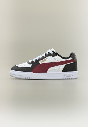 Low-top Puma sneaker met witte basis, zwarte overlays, een bordeauxrode zijstreep, witte veters en witte zool op een neutrale achtergrond.